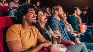 A row of people sitting in the cinema laughing and eating popcorn.